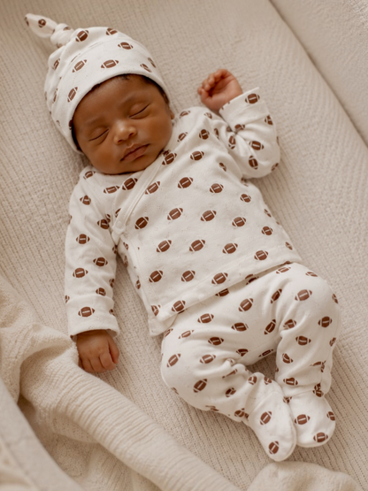 Sleeping baby in football-patterned pajamas and hat on a cozy blanket.