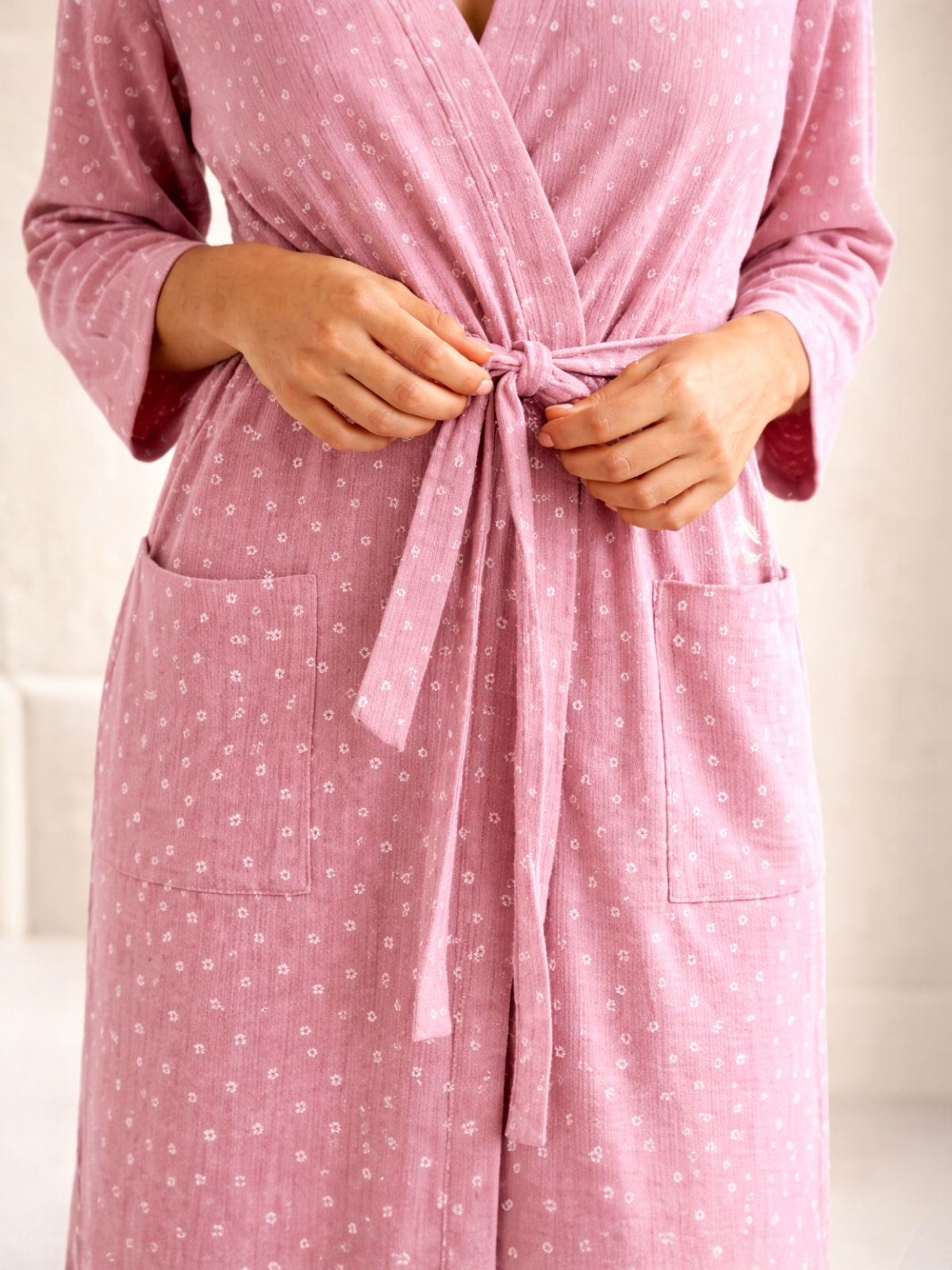 Woman tying a pink, floral patterned robe with pockets, focusing on her hands and the knot at the waist.