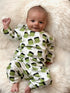 Smiling baby in green Frankenstein-themed pajamas, lying on a fluffy white blanket.