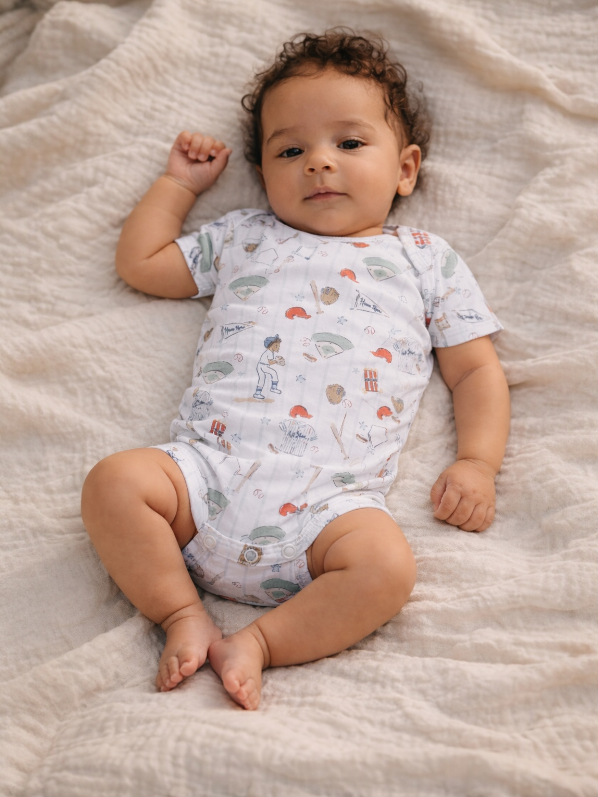 Baby lying on a blanket, wearing a playful patterned onesie with various colorful illustrations.