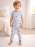 Smiling young boy in playful pajamas with cartoon patterns, standing in a bright, cozy bedroom.