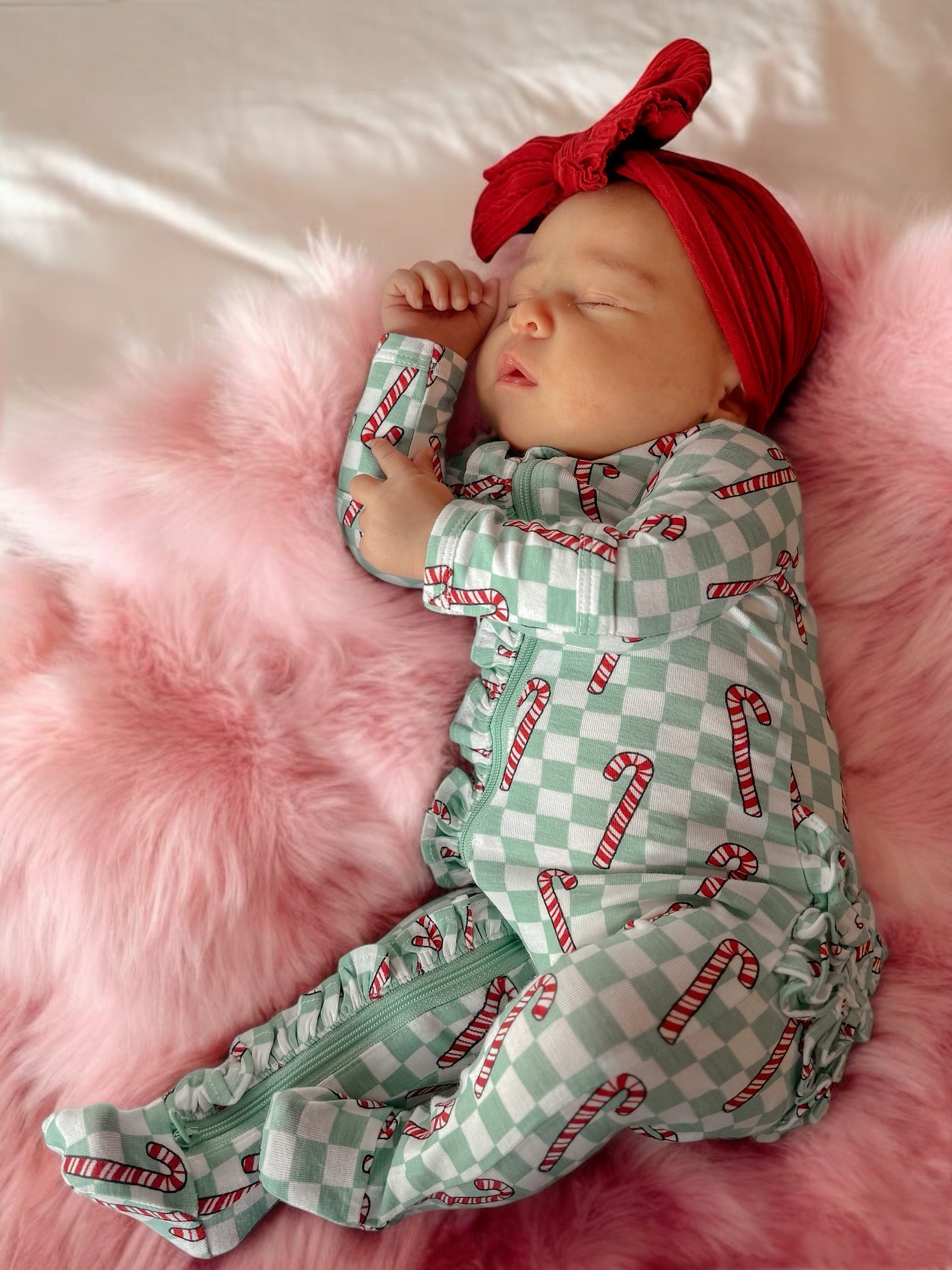 Sleeping baby in candy cane pajamas on soft pink fur blanket with a red headband.
