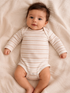 Smiling baby in a striped onesie lying on soft fabric backdrop, arms stretched out.