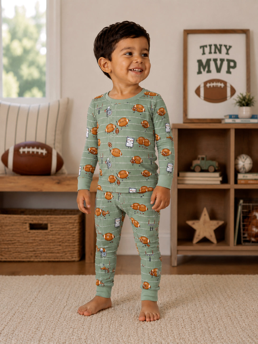 Smiling child in printed pajamas with playful designs, standing in a cozy living room with a football and decor.