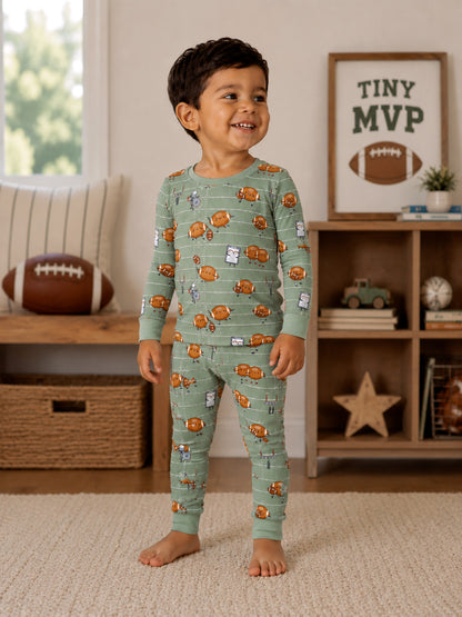 Smiling child in printed pajamas with playful designs, standing in a cozy living room with a football and decor.