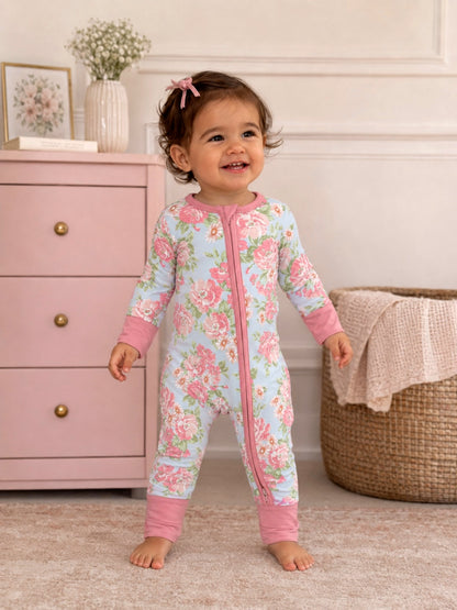 Smiling toddler in a floral onesie stands in a cozy room with pink dresser and braided basket.