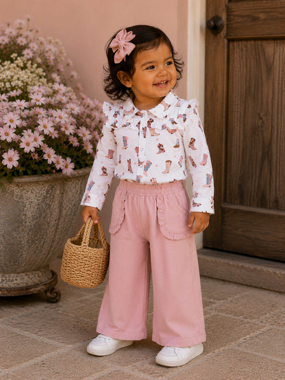 Smiling toddler in a white shirt with colorful boots and pink pants, holding a woven basket near flowers.