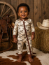 Smiling baby in horse-printed pajamas, standing on a cowhide rug with rustic decor in the background.