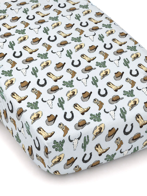 Light blue crib sheet featuring a western pattern of boots, hats, cacti, horseshoes, and cow skulls.