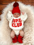 Baby wearing a cozy "Cupid Club" sweater, red hat, and booties, resting on a fluffy white blanket.