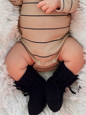 Close-up of a baby in a striped bodysuit and black knitted booties, resting on a fluffy blanket.
