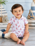 Smiling toddler in a lobster-patterned outfit, seated on a wooden floor with nautical decor in the background.