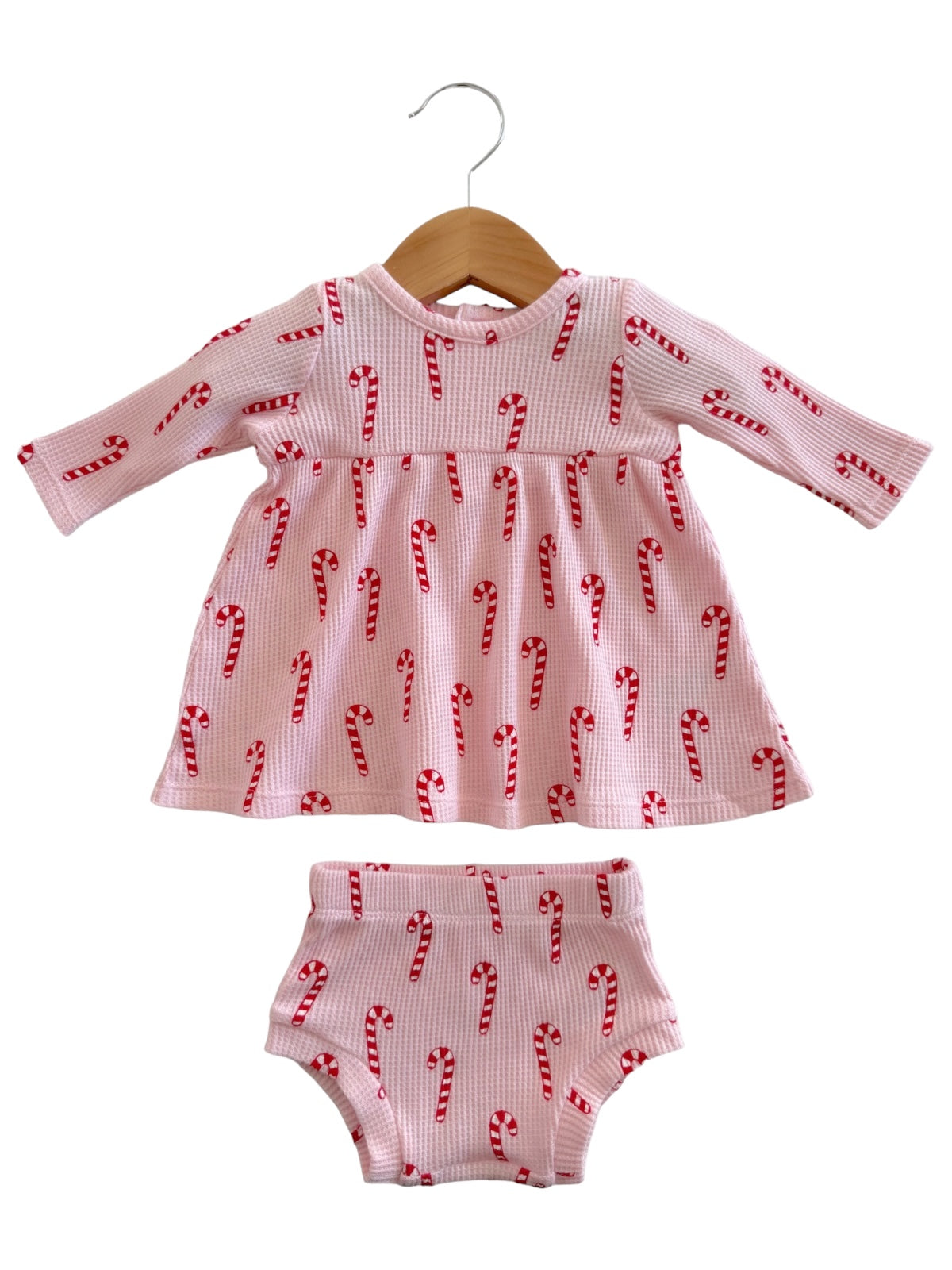 Candy cane patterned pink dress and matching shorts, hanging on a wooden hanger. Perfect for festive occasions.
