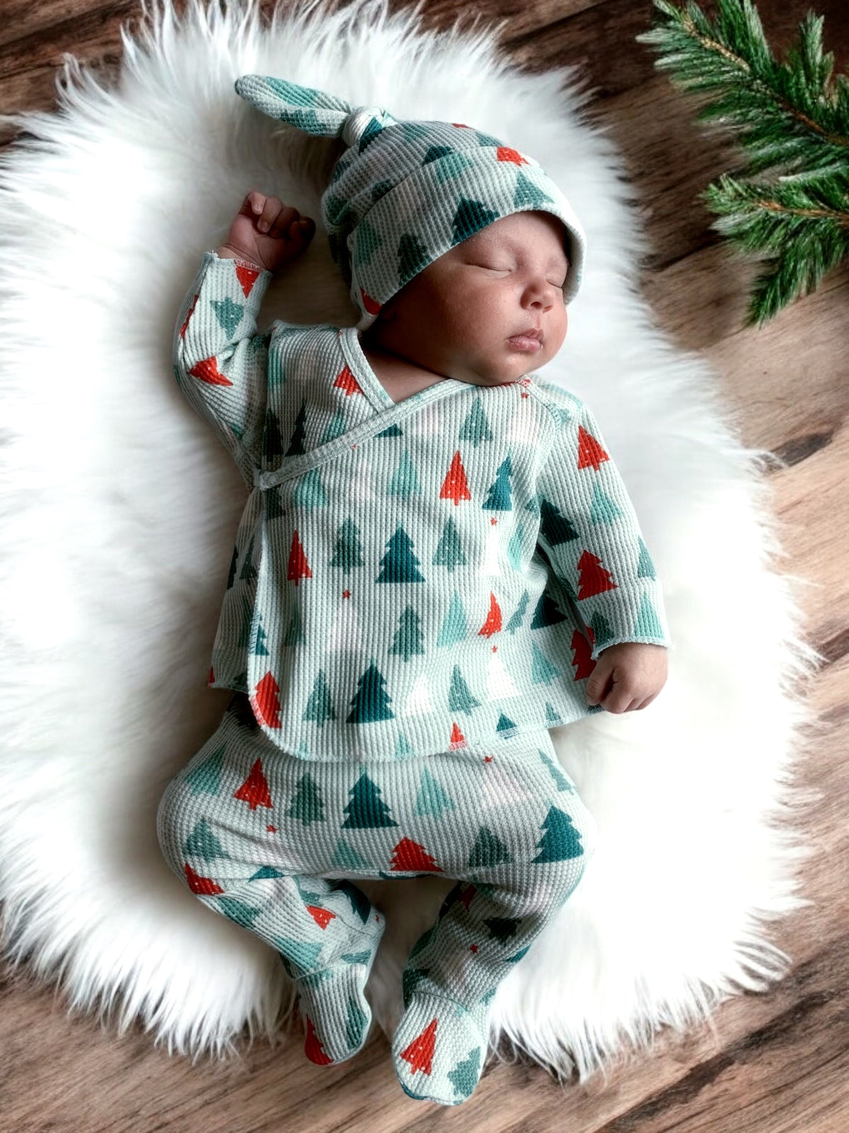 Baby peacefully sleeping on a soft rug, dressed in a festive, tree-patterned outfit and matching hat.