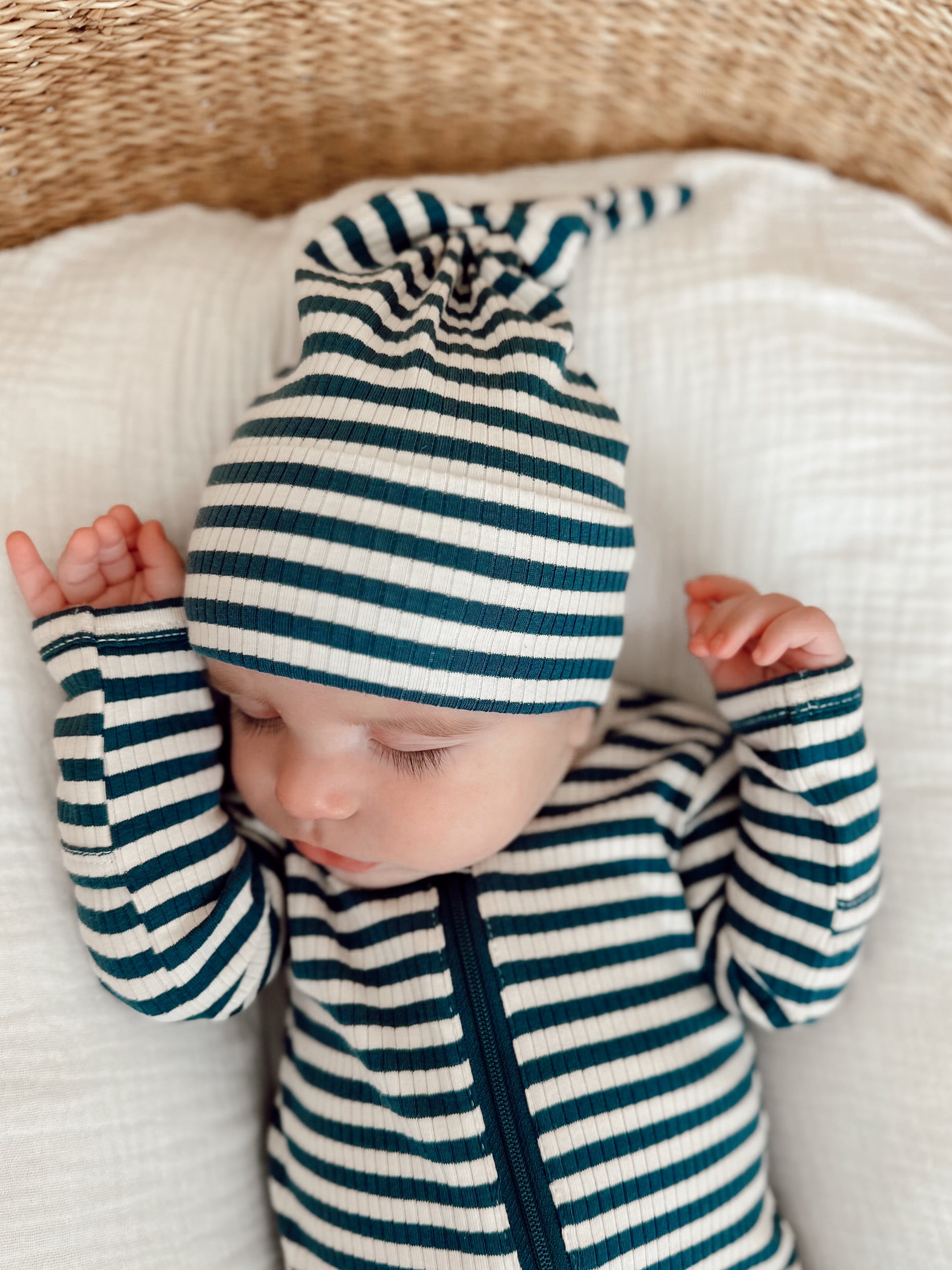Baby in a green and white striped outfit and hat, sleeping peacefully on a textured blanket.