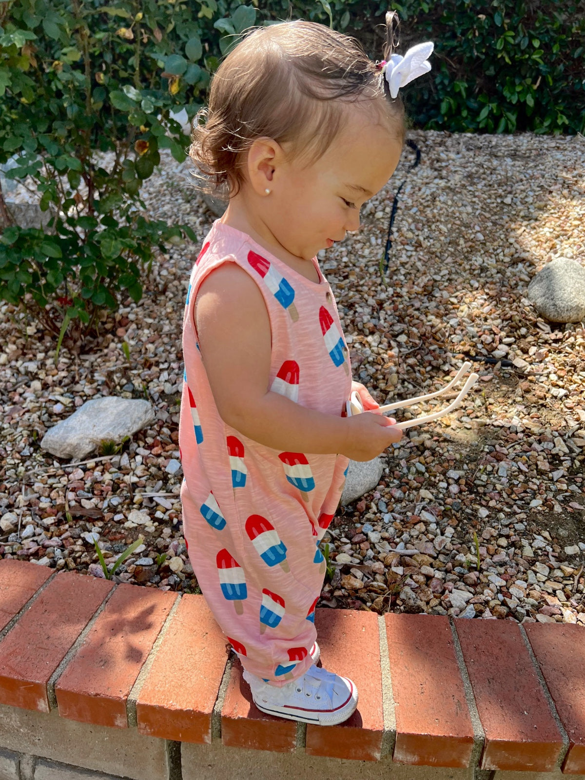 Toddler in a colorful popsicle-patterned outfit, playing outdoors on a sunny day.
