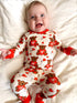 Smiling baby in bear-patterned pajamas, lying on a white blanket, with arms outstretched and joyful expression.