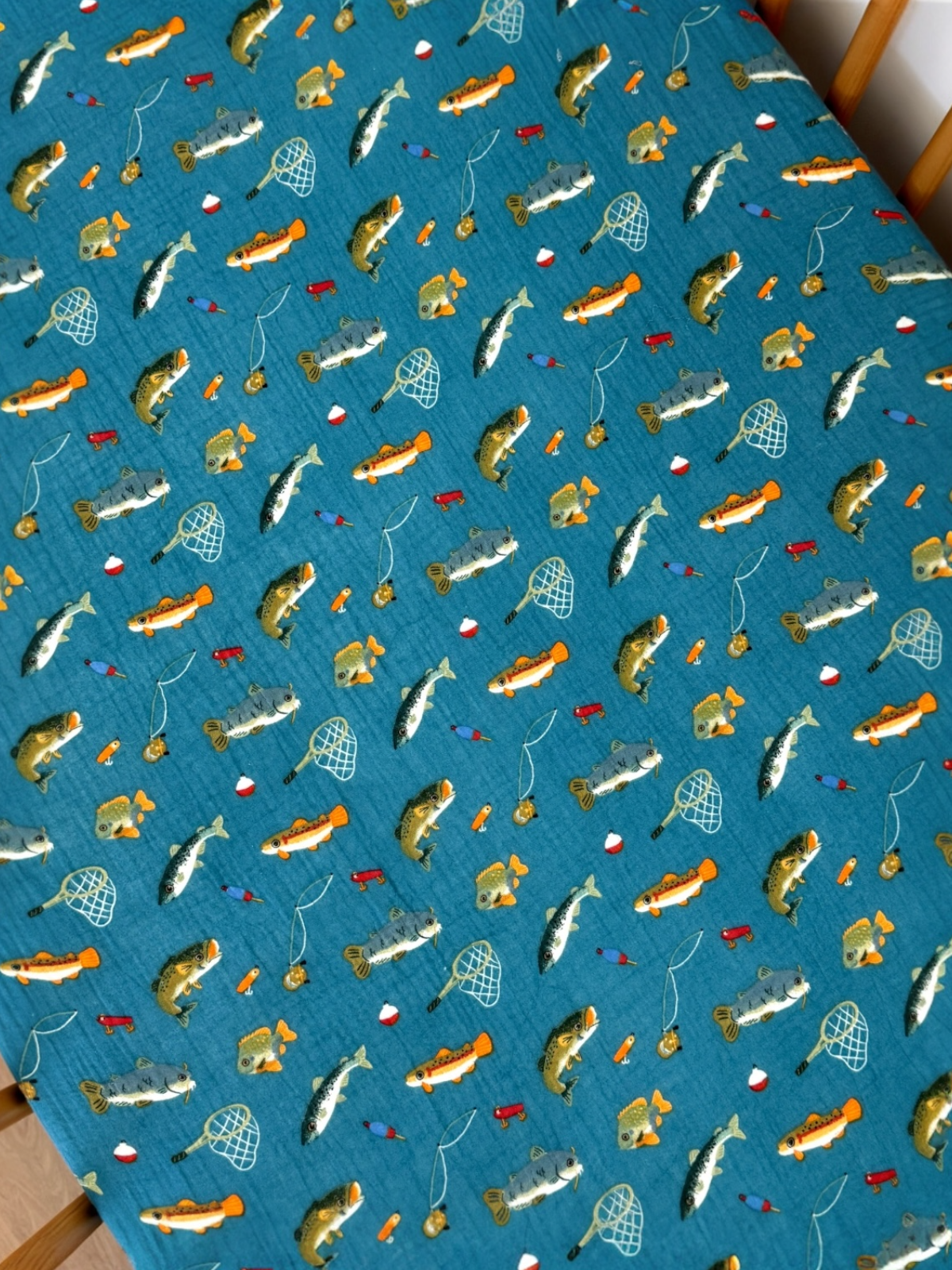 Patterned fabric featuring various fish, fishing nets, and lures on a teal background.