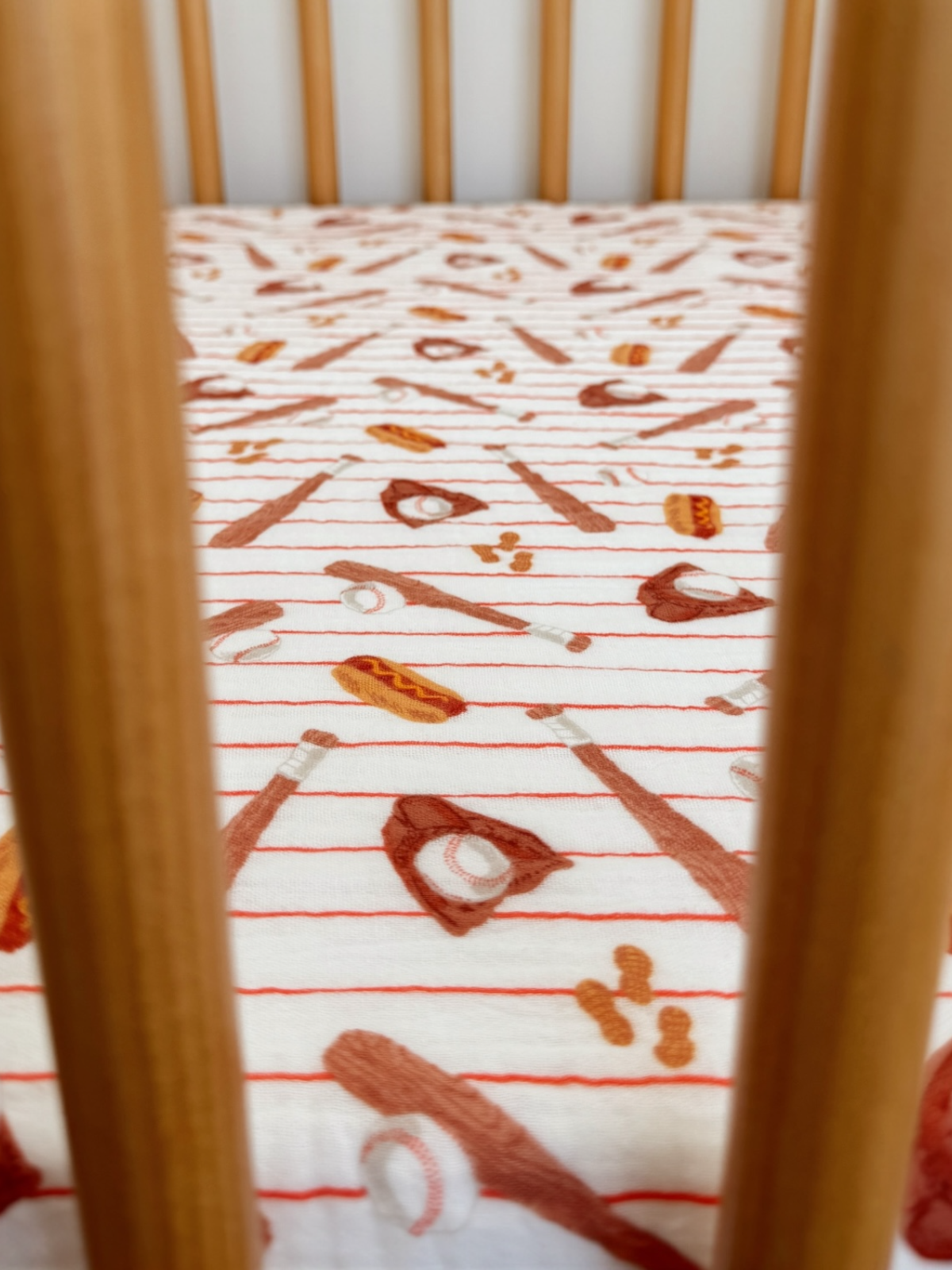 Crib bedding with playful sports-themed embroidery. Wooden slats frame the view.