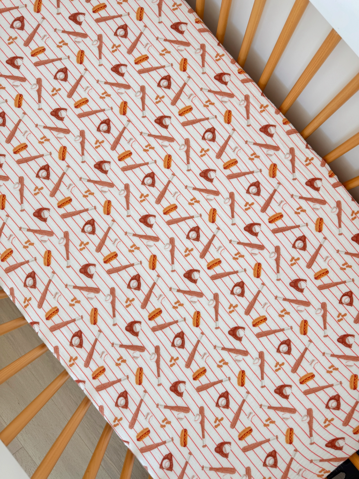 Crib sheet with playful kitchen-themed pattern featuring utensils and baked goods in warm tones.