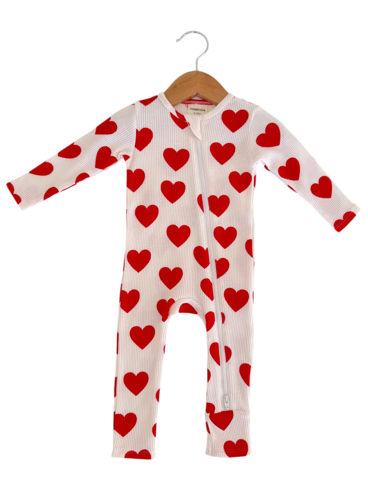 White onesie with red heart patterns, hanging on a wooden hanger against a plain background.