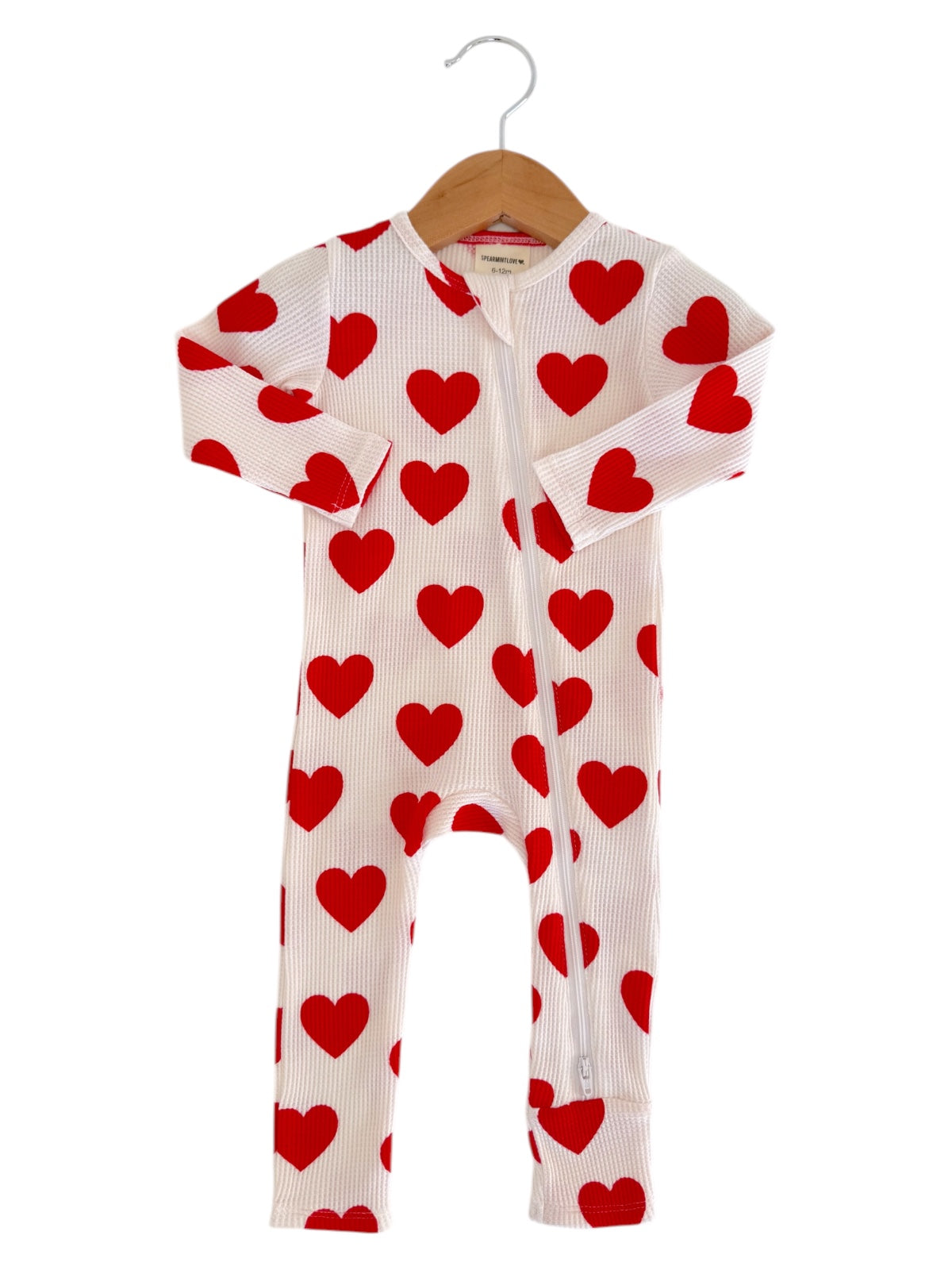 White onesie with red heart patterns, hanging on a wooden hanger.