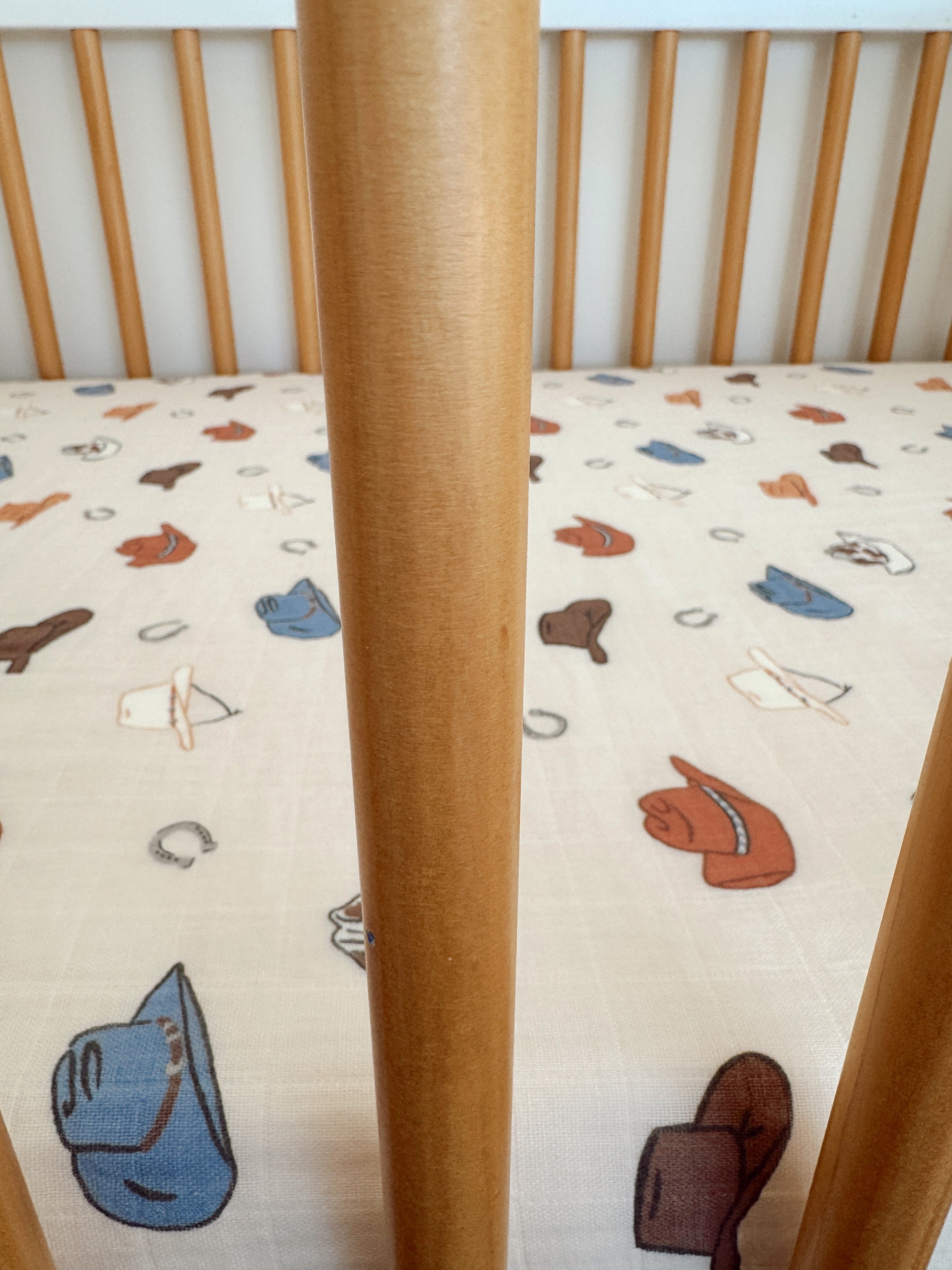 Crib with wooden slats featuring a playful hat-patterned bedding.