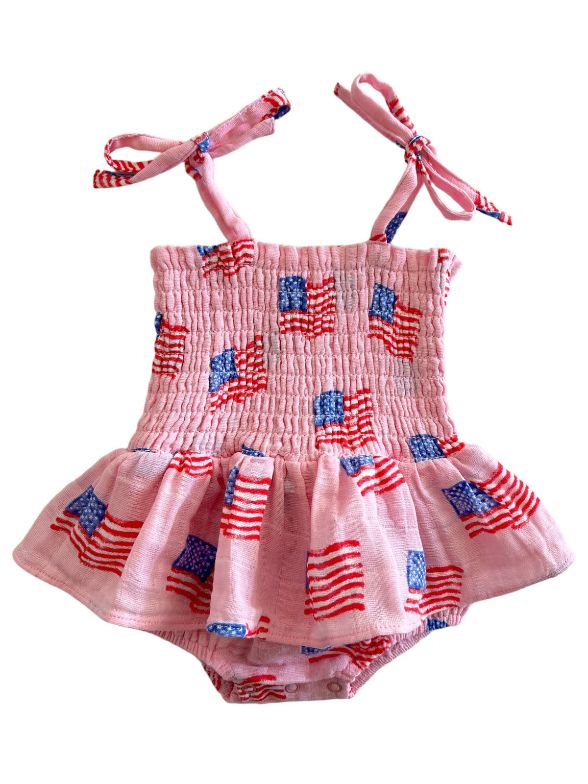 Pink baby romper with smocked bodice and American flag patterns, featuring tie straps and a flared skirt.