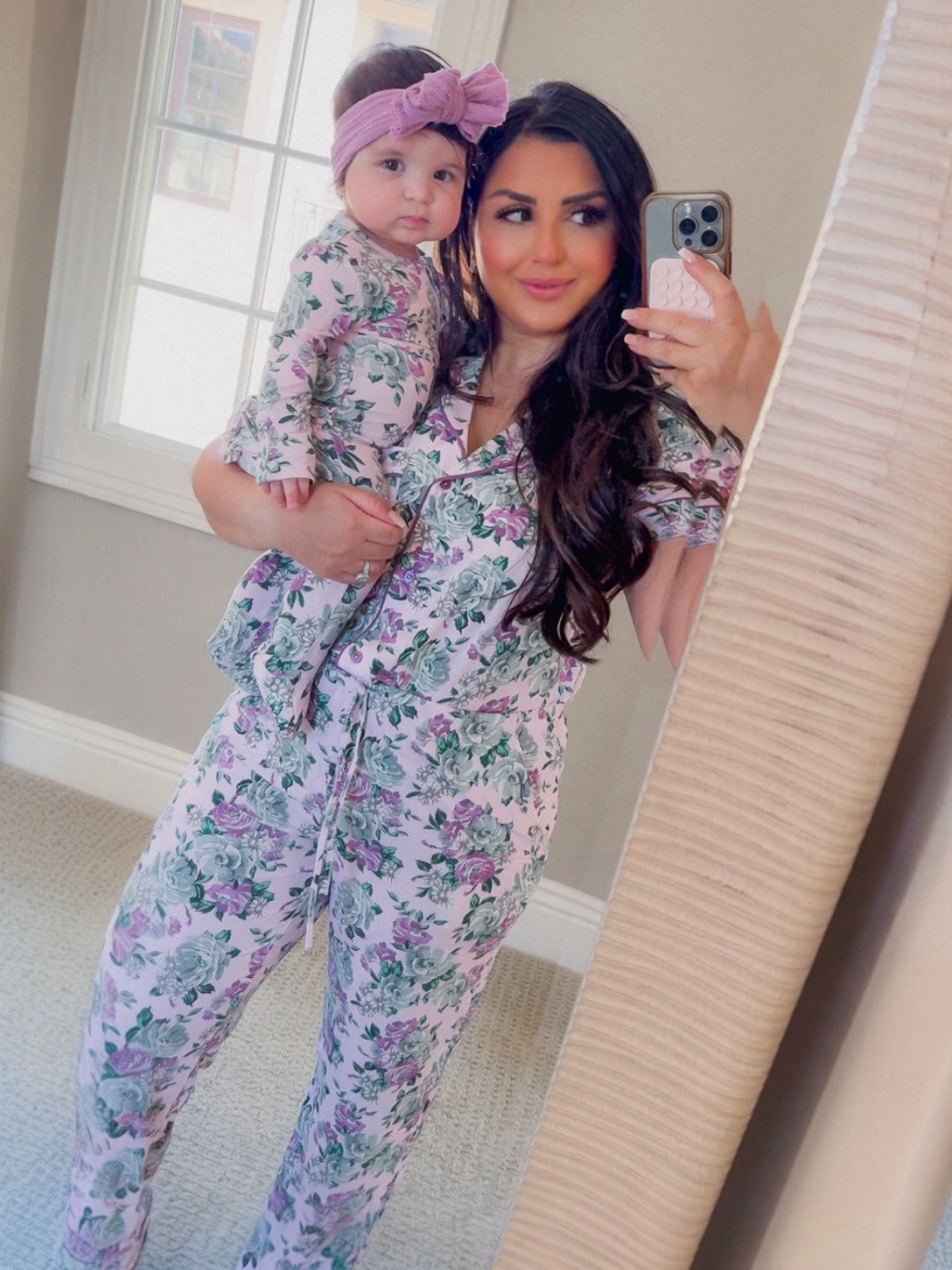 Mother and child in matching floral pajamas, smiling in a mirror selfie at home.