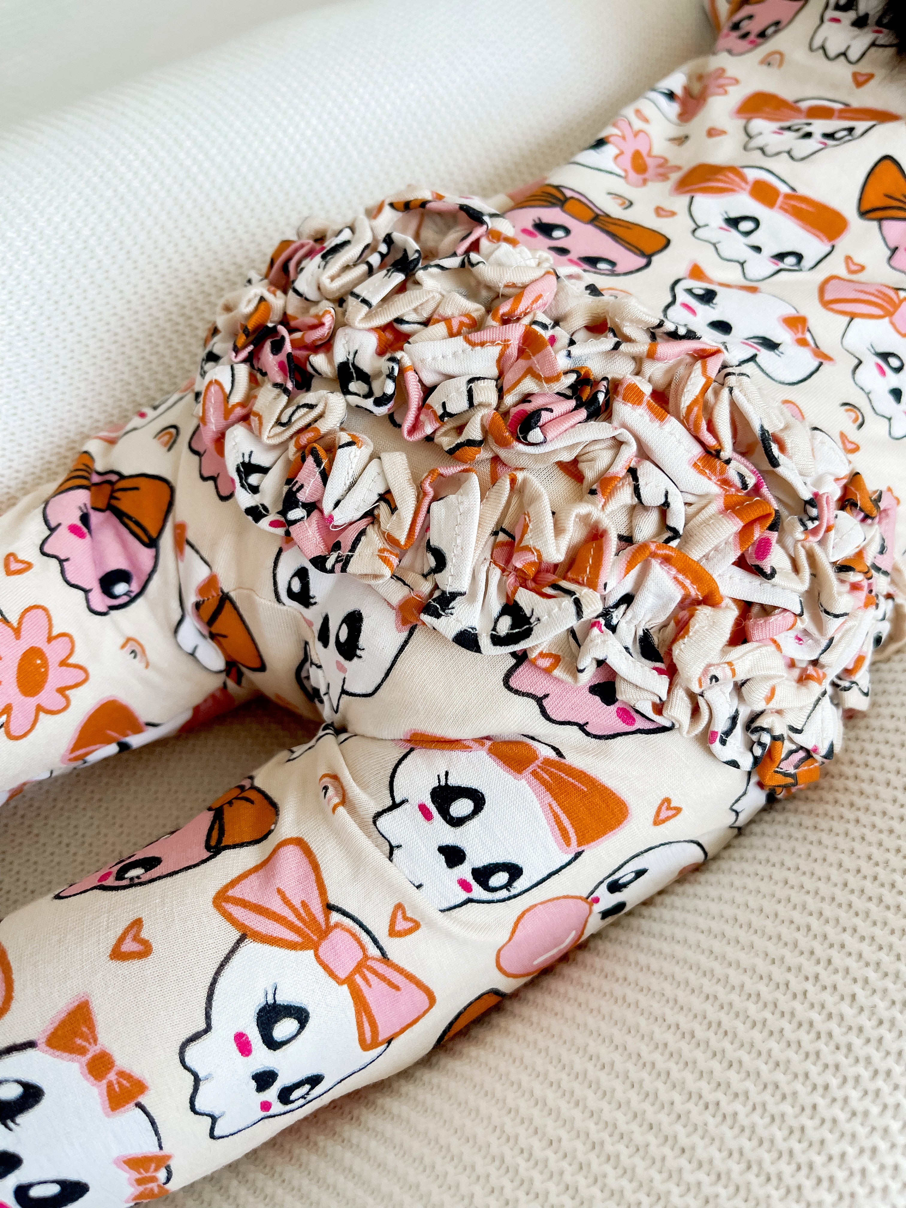 Child's leggings with a playful cat print and ruffled detailing in soft pastel colors.