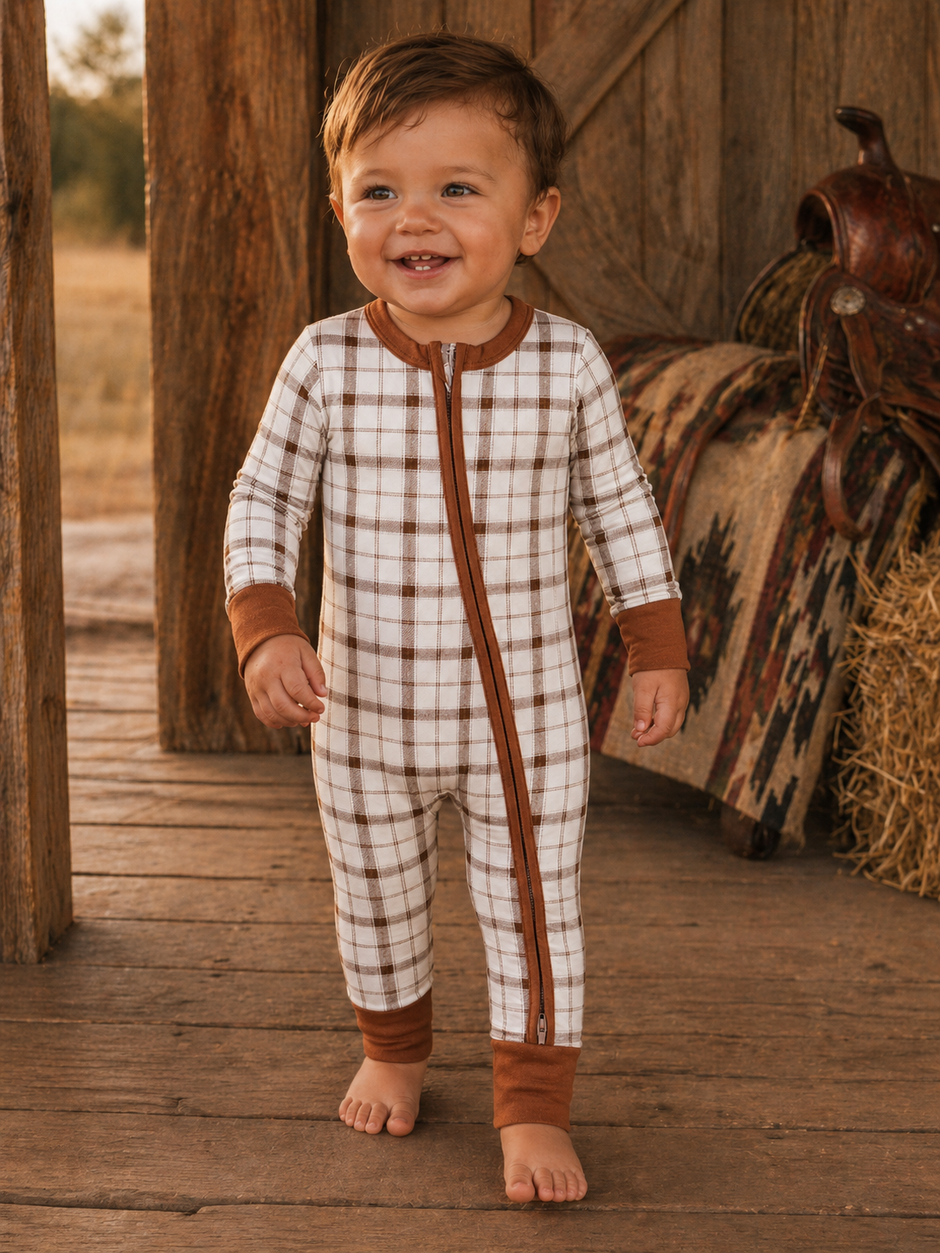 Smiling toddler in a cozy plaid onesie standing on wooden floor in a rustic setting.