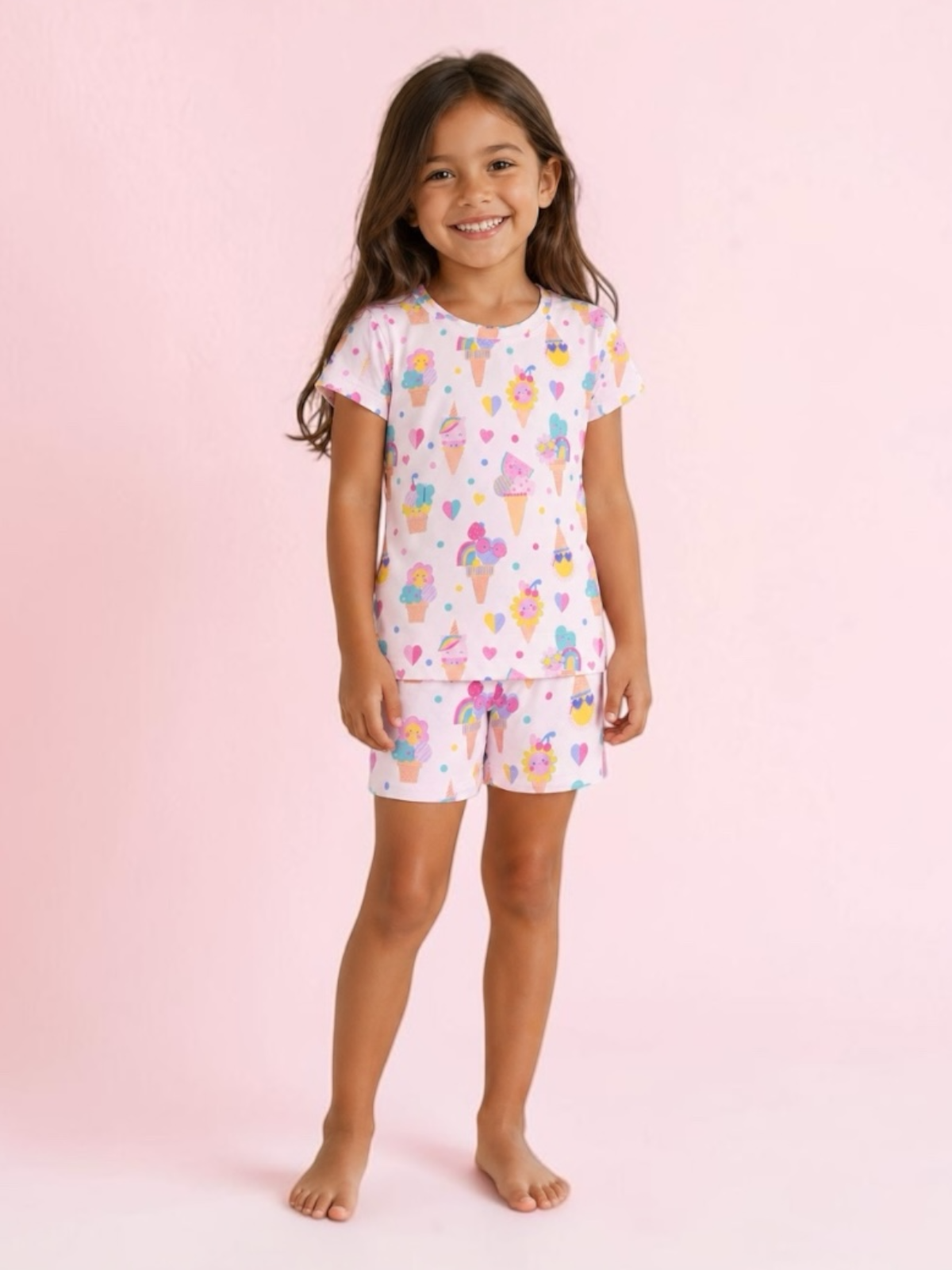 Smiling girl in colorful ice cream-themed pajamas against a pink background.