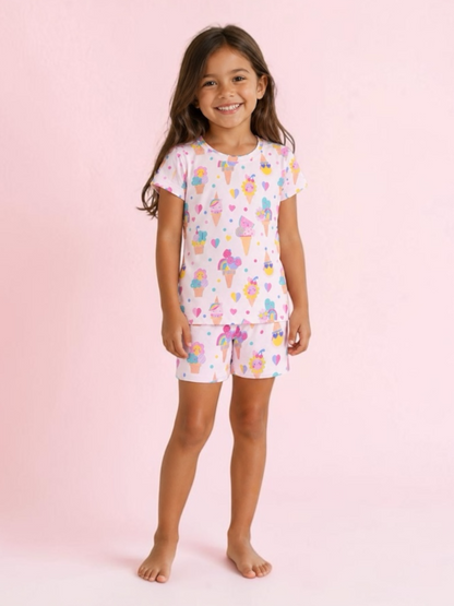 Smiling girl in colorful ice cream-themed pajamas against a pink background.