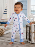 Happy toddler in a boat-patterned pajama, standing on wooden floor near toys and decor in a bright, airy room.