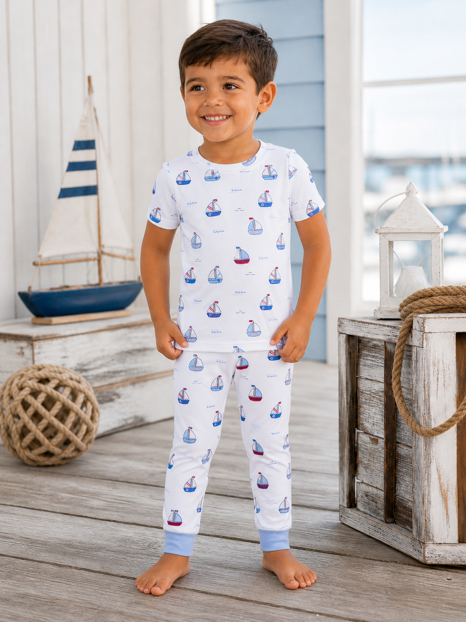 Smiling child in nautical-themed pajamas, standing by a sailboat and wooden decor in a coastal setting.