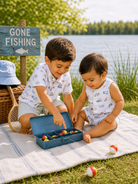 Two young boys play with colorful toy fishing supplies near a "Gone Fishing" sign by a lake.