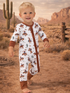 Smiling child in cowboy-themed pajamas, standing in a desert landscape with cacti and mountains.