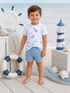 Smiling boy in beach attire stands near a lighthouse and lifebuoy, with ocean in the background.