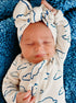 Baby asleep on blue blanket, wearing a cloud-patterned outfit and a large bow headband, with a peaceful expression.