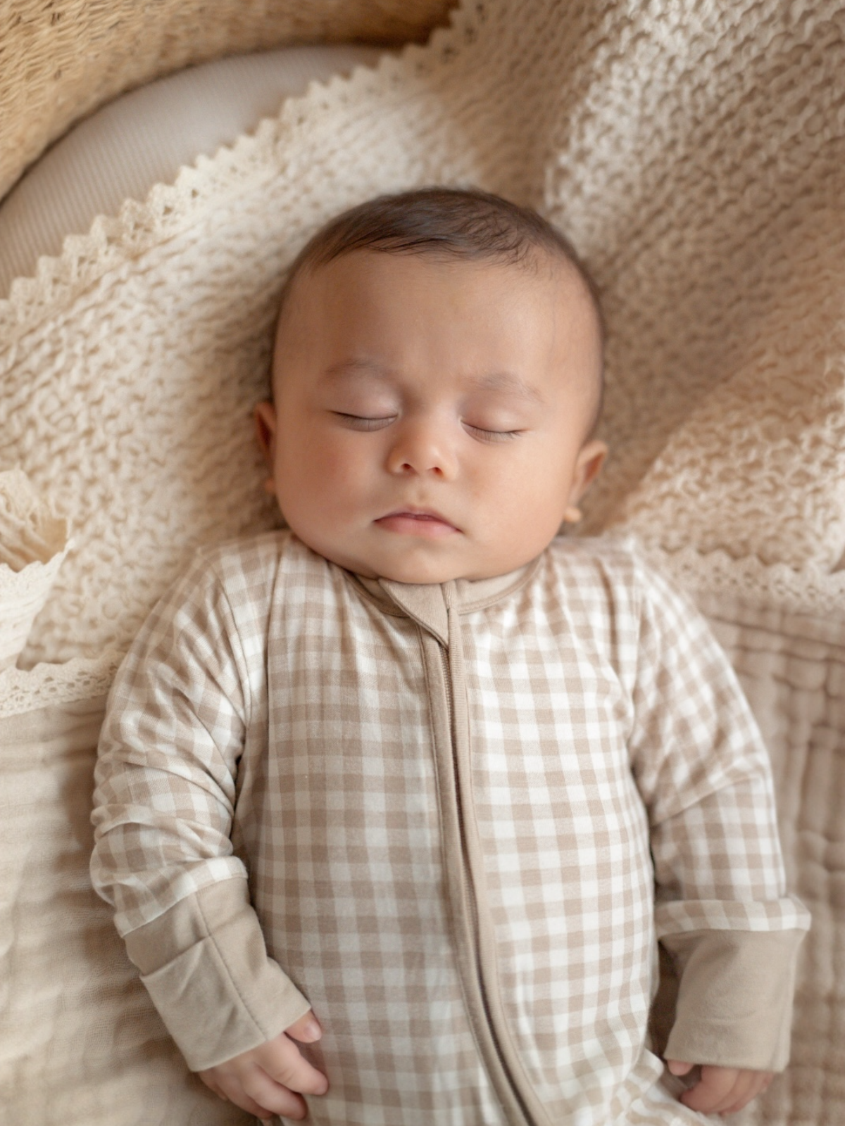 Sleeping baby in a checkered outfit resting on a cozy blanket. Soft, warm colors create a peaceful atmosphere.