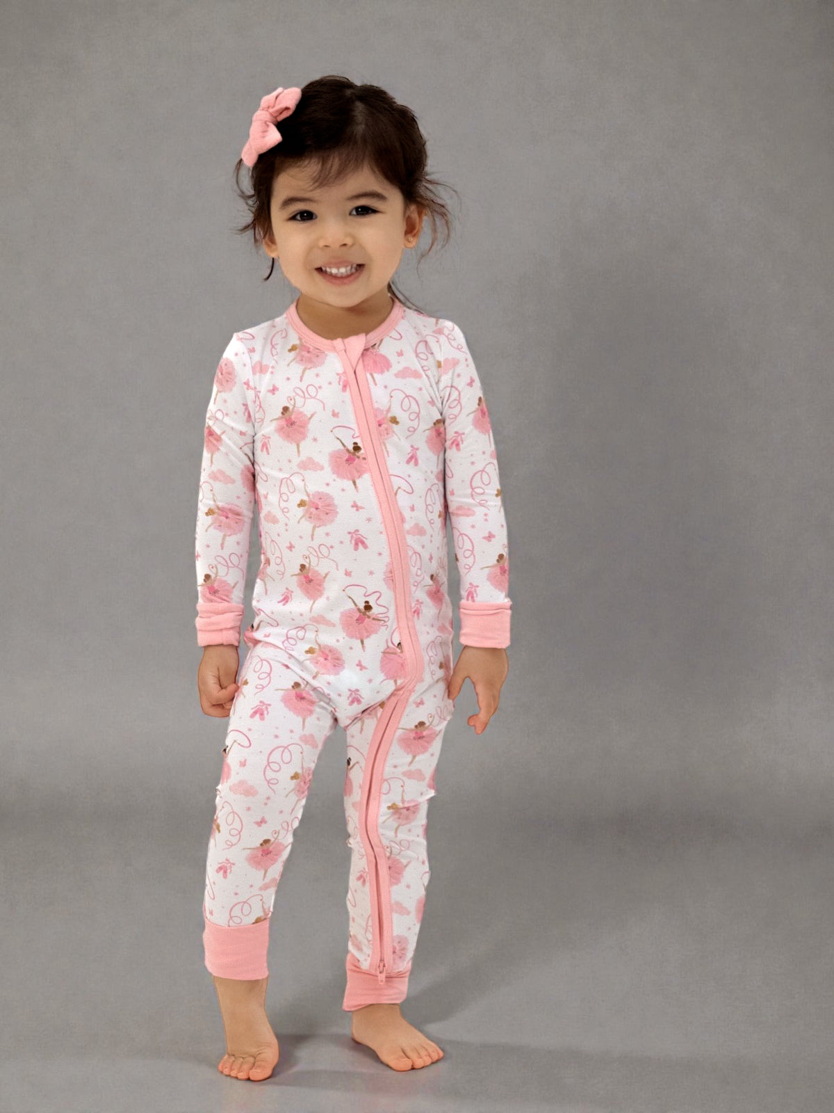 Smiling child in pink floral pajamas with a bow, standing on a gray background.