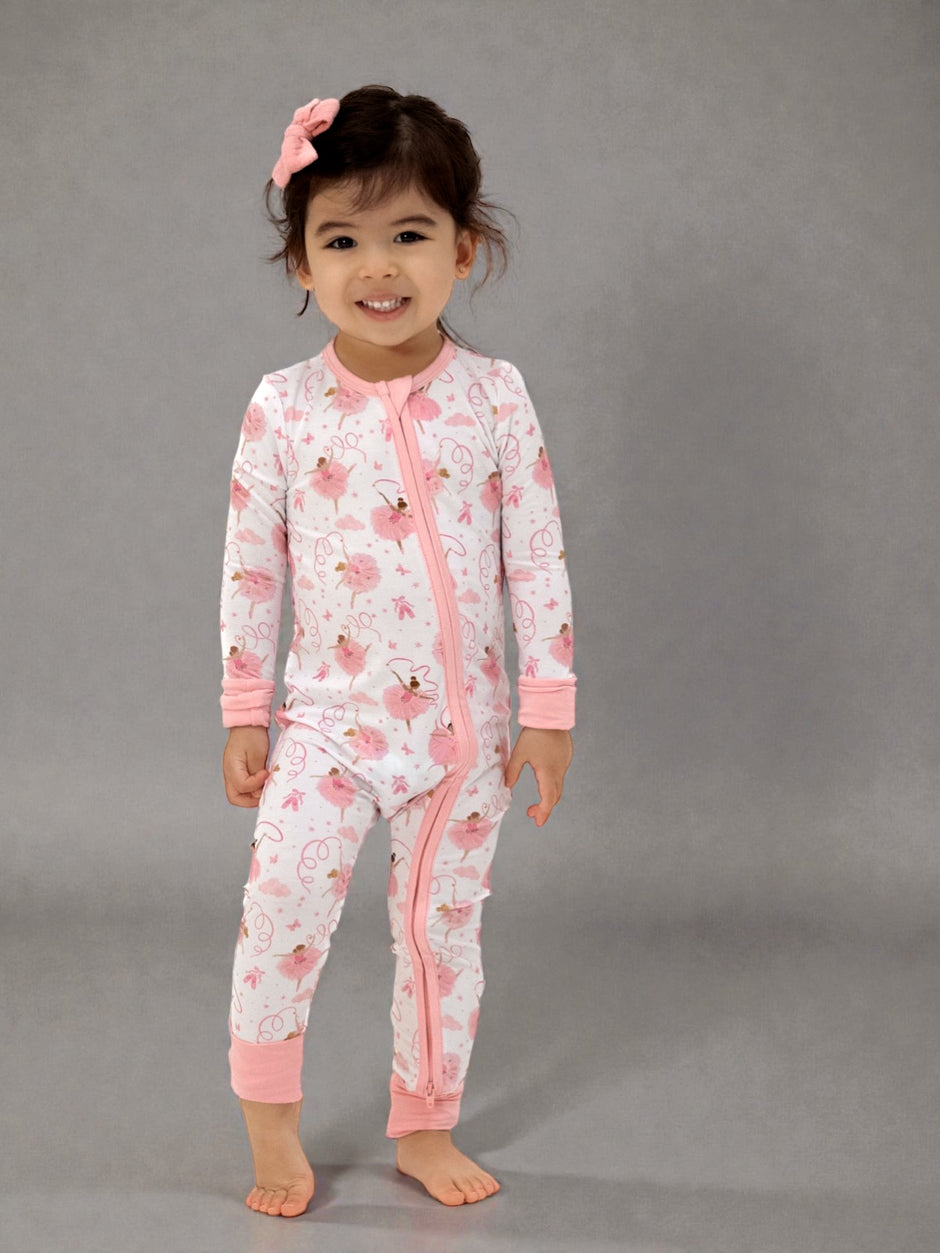Smiling child in pink floral pajamas with a bow, standing on a gray background.