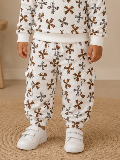 Child wearing a white outfit with a colorful butterfly pattern and white sneakers, standing on a textured rug.