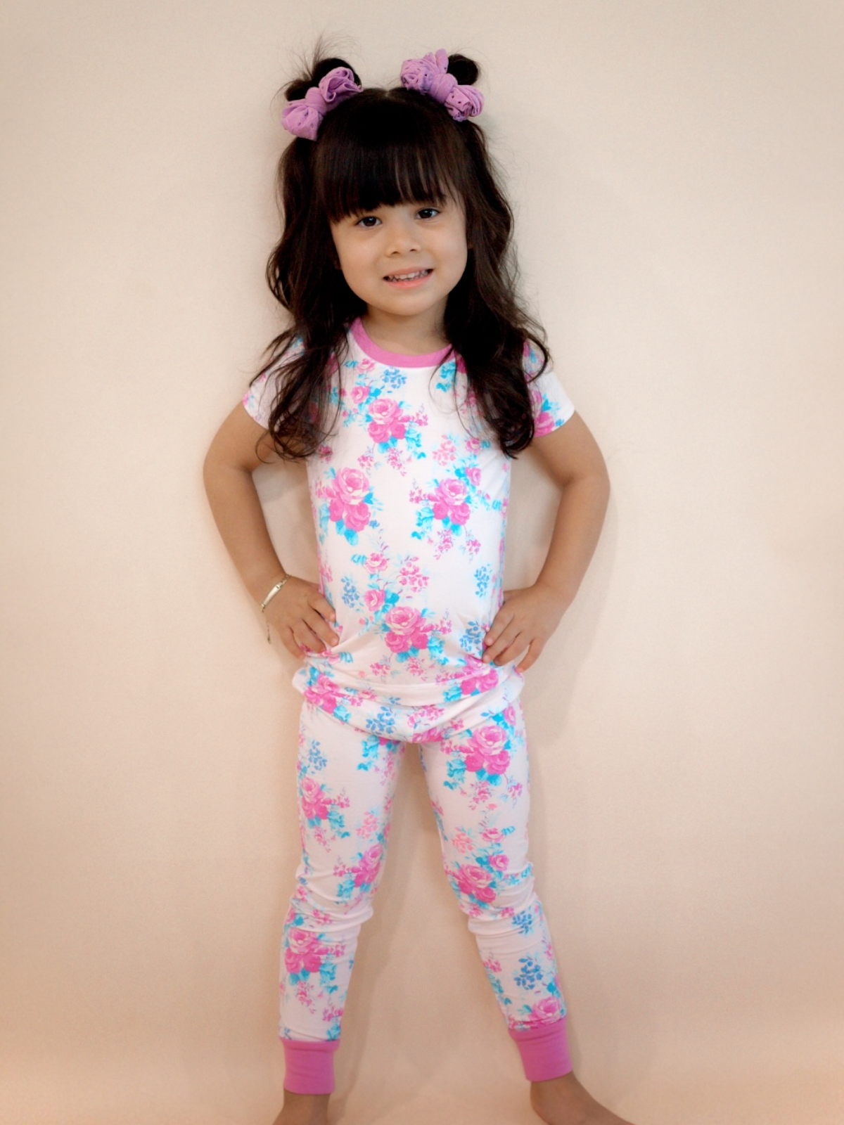 Smiling girl in floral pajamas with purple accents, posing confidently against a neutral background.