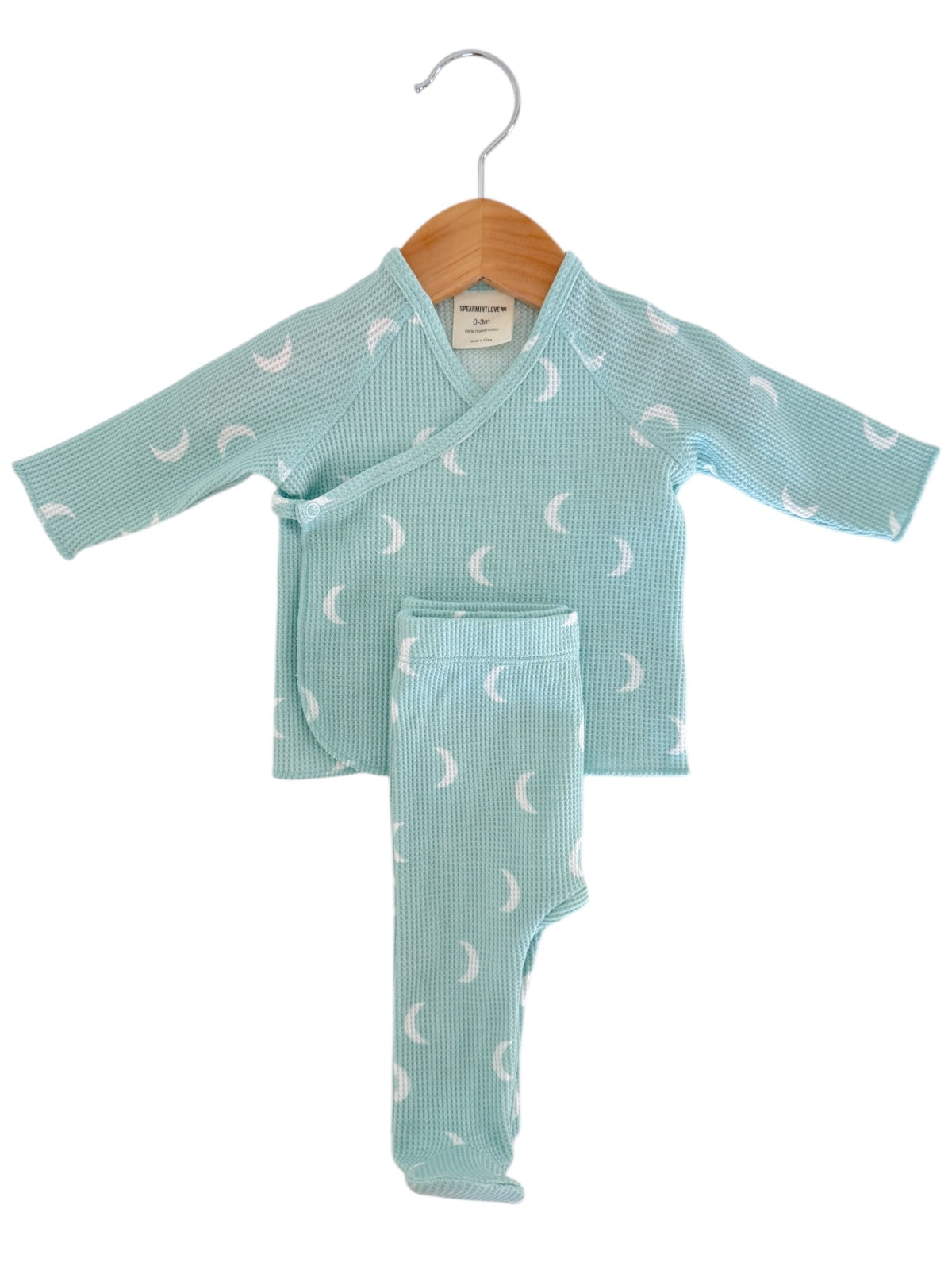 Mint green baby outfit with white crescent moon pattern hanging on a wooden hanger.