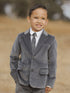 Smiling boy in a gray suit standing outdoors against a blurred natural background.