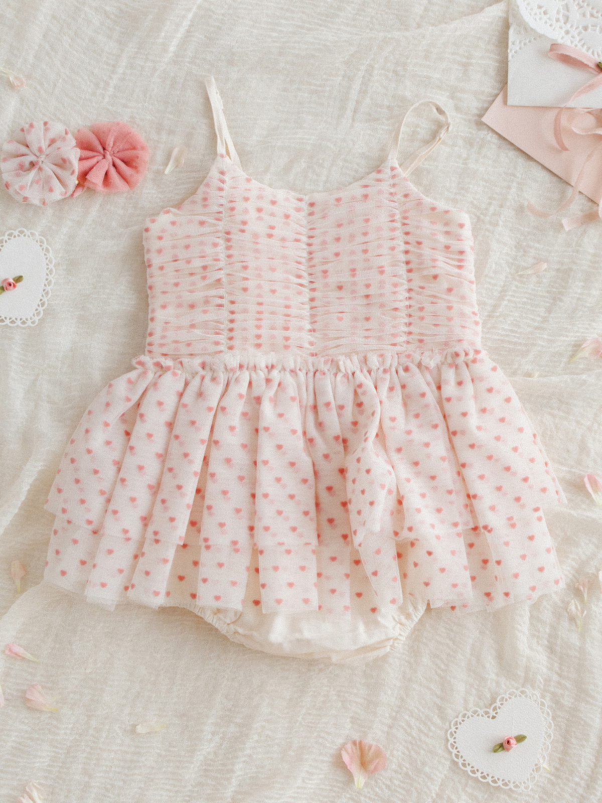 Pink and white toddler dress with heart patterns, surrounded by fabric flowers and decorative accents on a soft background.