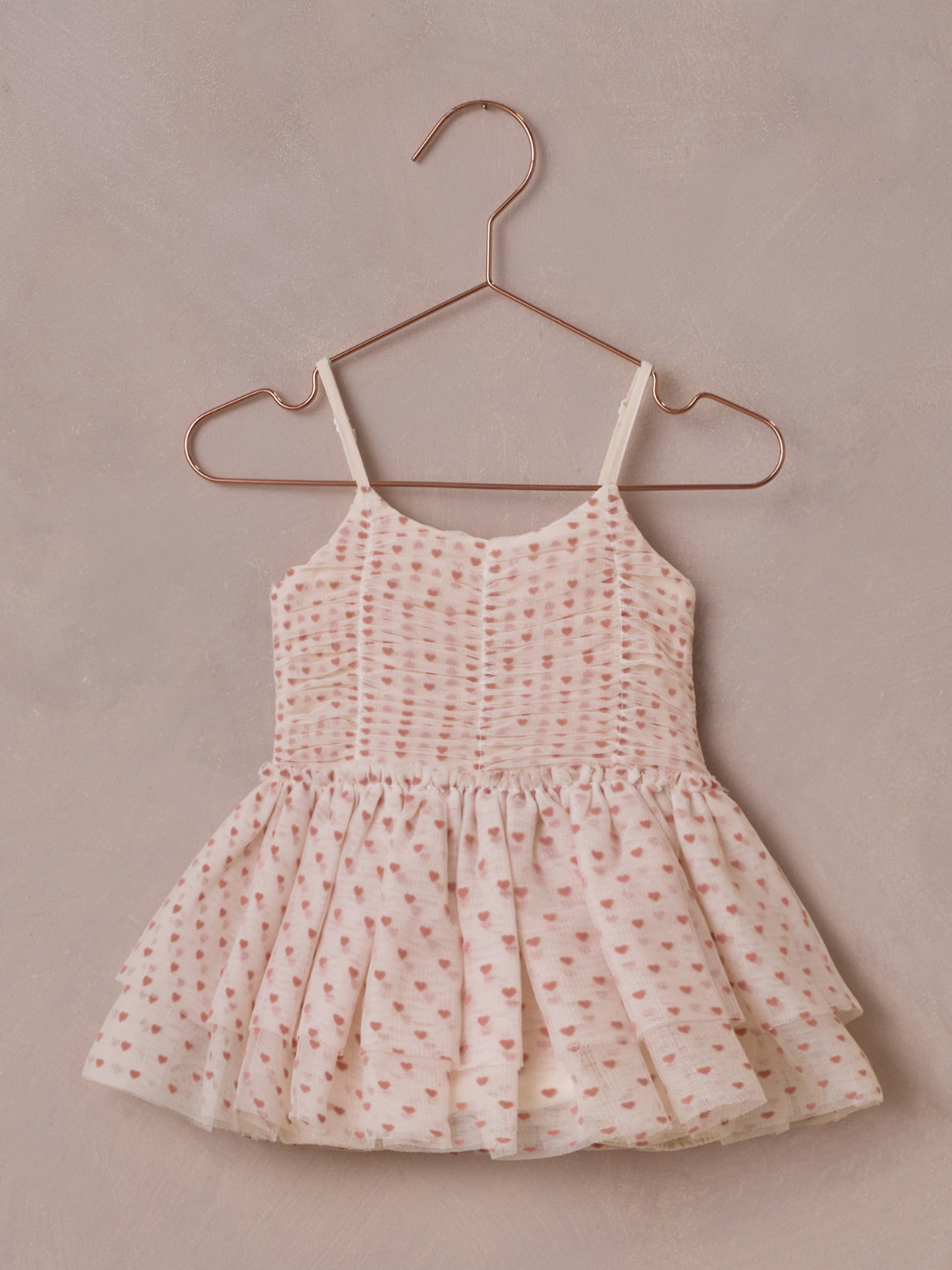 Light pink dress with heart patterns, hanging on a copper hanger against a textured background.