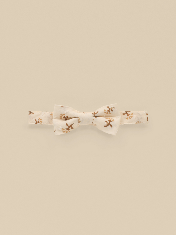 Cream bow tie with brown floral pattern on a beige background.