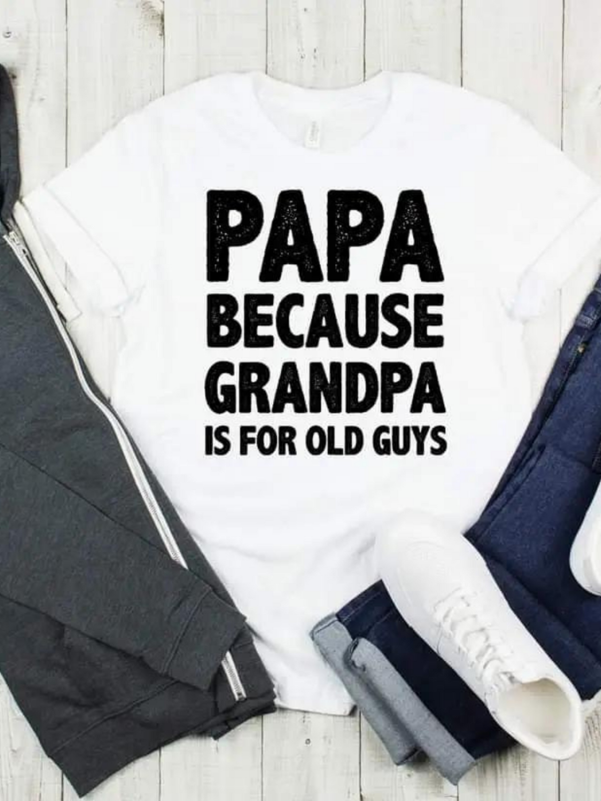 White t-shirt with "PAPA BECAUSE GRANDPA IS FOR OLD GUYS" printed in bold black letters, styled with casual clothing.